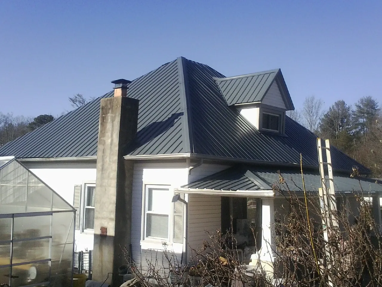 Dark blue standing seam metal roof on a white farmhouse with dormer — Slate & Tile Roof Repair by Roofing Brothers in Bondurant