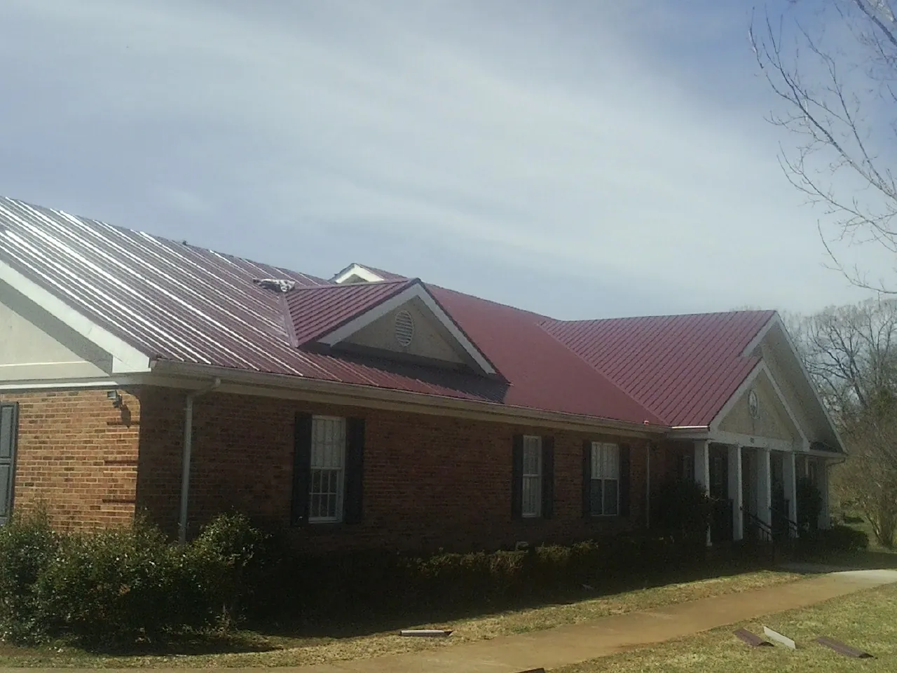 Red metal roof with gabled entries on a long brick building, from a Hail Damage Roof Repair job in Bondurant