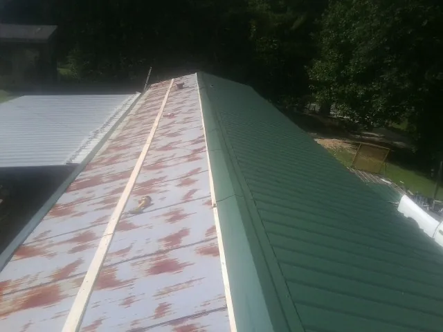 Old rusted panels beside newly installed green metal roofing — Wind Damage Roof Repair by Roofing Brothers in Bondurant
