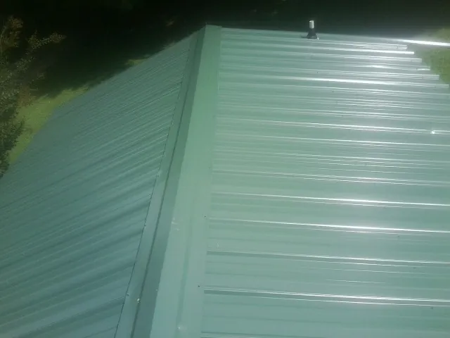 New green metal panels meeting at the ridge of a roof — Flat Roof Repair work by our crew in Bondurant