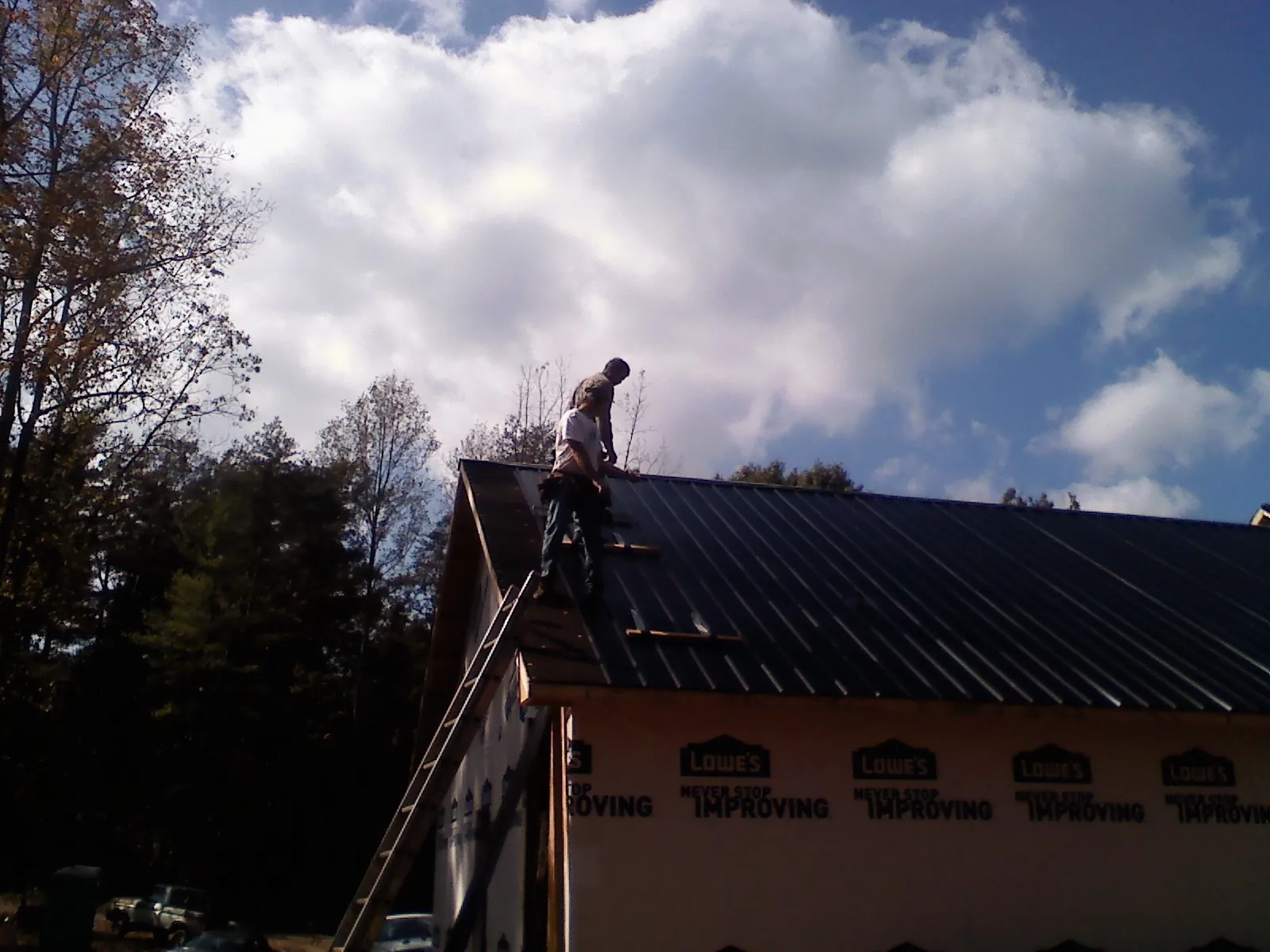 Roofer fastening dark metal panels high against a cloudy sky, from a Roof Inspection job in Bondurant