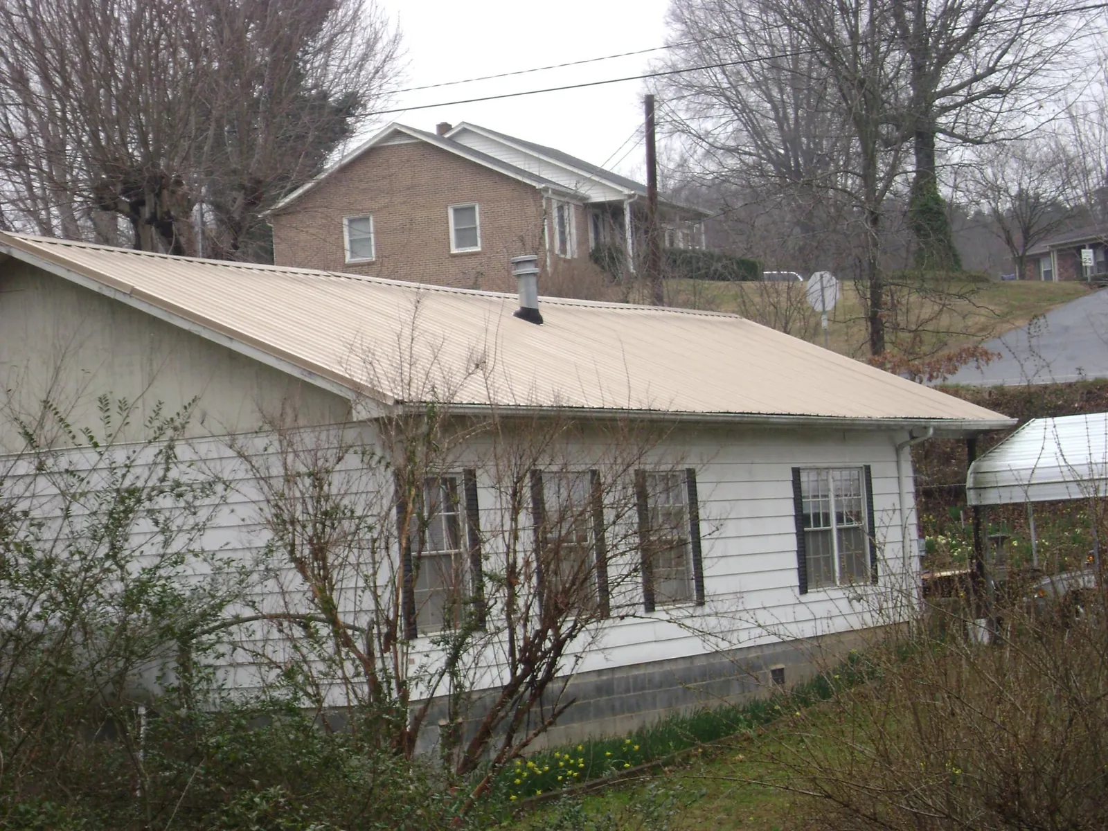 Tan metal roof on a white sided house set into a hillside — Commercial Roofing by Roofing Brothers in Bondurant