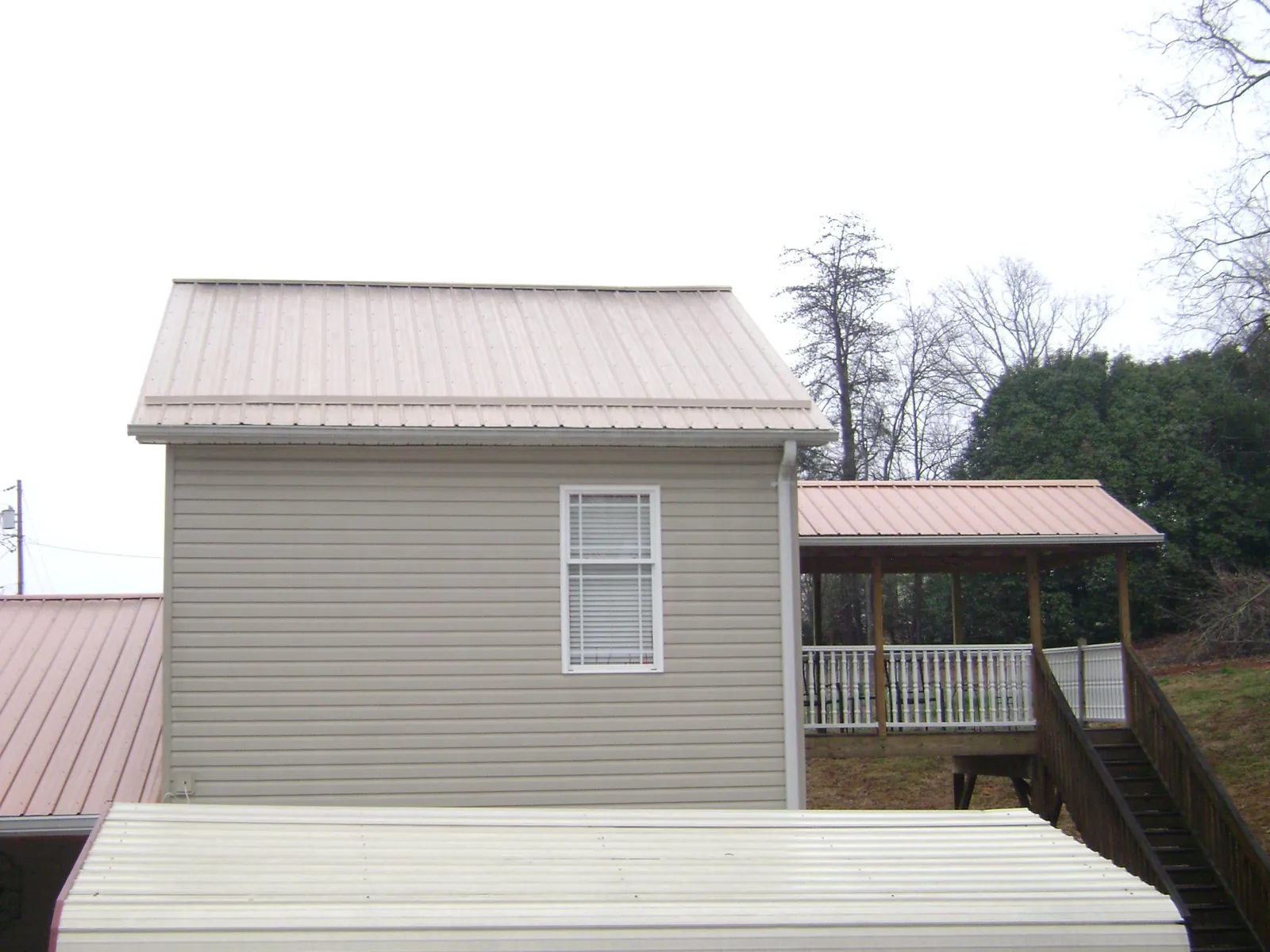 Tan metal roofs on a two story addition and attached porch, from a Roof Replacement job in Bondurant