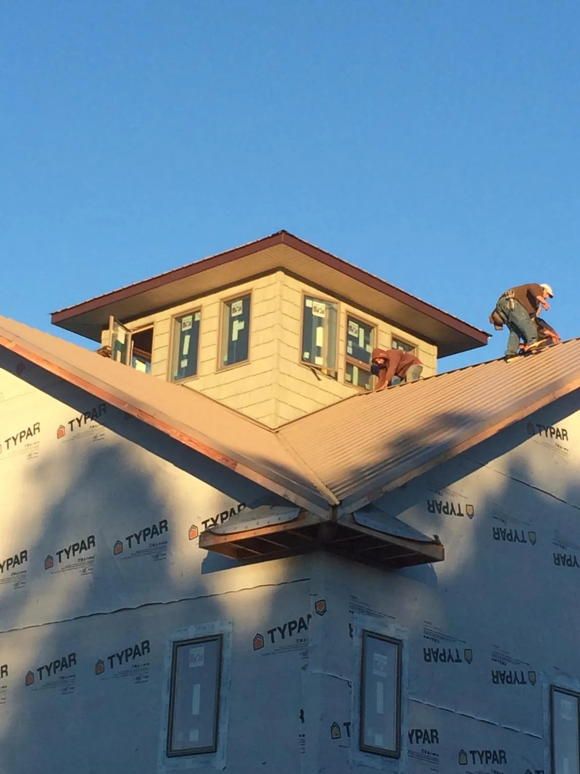 Roofers working around a rooftop cupola on a new metal roof at sunset — Roof Waterproofing in Bondurant by Roofing Brothers